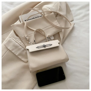 Détail d'un sac à main crème avec fermoir rotatif métallique sur fond de blazer beige