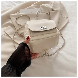 Detail of cream quilted mini backpack with silver chain strap on white blazer