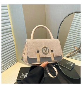 Detail of beige flap bag with woven texture, metal M buckle and elegant top handle