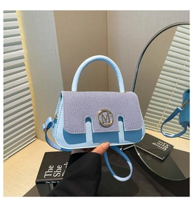 Close-up of light blue leather handbag with striped fabric and gold M-shaped metal clasp