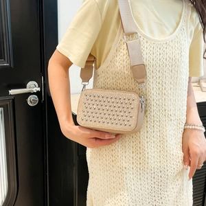 Beige textured crossbody bag with silver stud details and wide strap on model