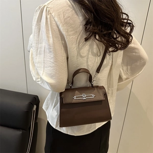 Sac bandoulière en cuir marron foncé avec boucle argentée porté par un mannequin femme