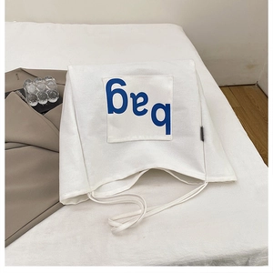 Detail of white canvas tote bag featuring a blue bag letter patch and shoulder strap