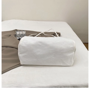 Close-up of a white canvas tote bag with slim handles placed on soft fabric background