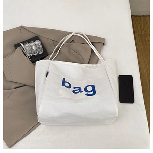 Detail of white canvas tote bag with front pocket featuring blue bag text and durable straps