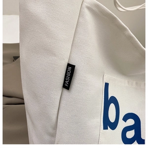 Detailed close-up of thick beige canvas tote showing side logo and blue letter print