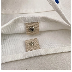 Detail of silver metal snap button closure and thick canvas texture on white tote bag