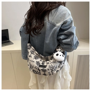 Side view of printed canvas crescent tote bag with panda pendant shown on a person