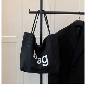 Detail view of large black canvas tote bag with white bag print and fashion woven label