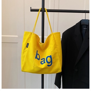 Detail of yellow canvas tote bag featuring blue bag print and fashion side label
