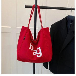 Close-up of red canvas tote bag featuring a white letter print and side label detail
