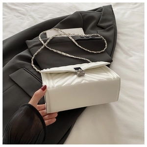 Detail of white V-quilted small square bag with silver metal lock and chain strap