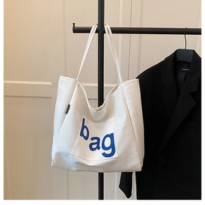 Detailed view of white canvas tote bag with blue bag lettering and external pocket