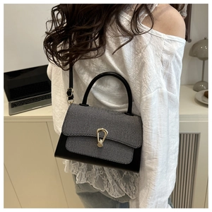 Detail of a two-tone crossbody bag featuring a U-shaped gold buckle and a curved handle