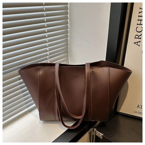 Detail of dark brown leather tote bag with embossed Fashion text in natural sunlight