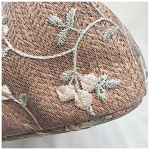 Detailed view of woven straw bag with floral embroidery and white mesh overlay