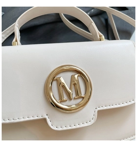 Gros plan du sac à main beige en cuir avec logo M doré et détails de couture