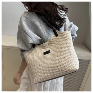 Close-up of off-white woven tote bag featuring herringbone texture and black leather label
