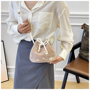 Close-up of pink woven bucket bag with floral embroidery and white drawstring closure