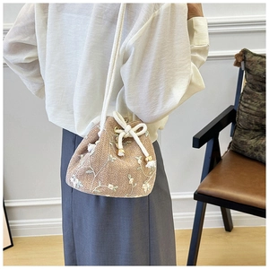 Close-up of pastoral woven bucket bag with floral embroidery and tassel drawstring detail