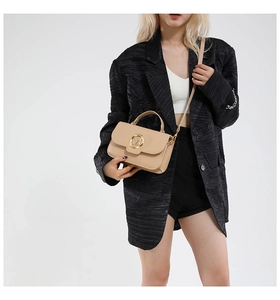 Mini sac beige tendance avec logo M doré porté par un mannequin en tailleur noir chic