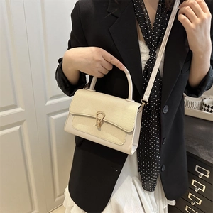 Elegant cream square crossbody bag with gold buckle shown on a model in a modern room