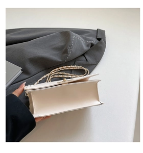 Detail of white leather crossbody bag with gold chain strap and accordion side structure