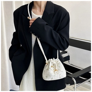 Detail of white woven bucket bag with drawstring closure and gold metallic beads