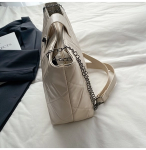 Detail of beige quilted tote bag featuring metal chain handles and leather shoulder strap