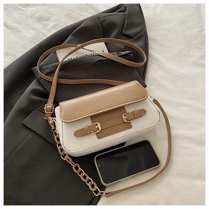 Detail of small crossbody bag with metal buckles and chain decoration against a blazer