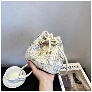 Detail of hand-woven drawstring bucket bag with floral embroidery and tassel accents