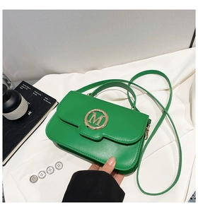 Détail d'un sac à main vert avec boucle dorée en M et fine bandoulière amovible
