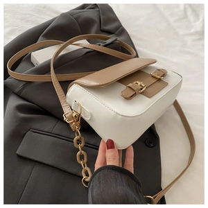 Detail of color-block PU leather shoulder bag with gold buckles on a grey blazer