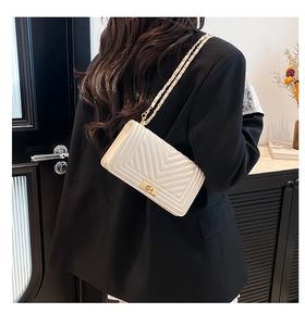 Detail showing an ivory square chain bag with chevron quilting and golden turn-lock