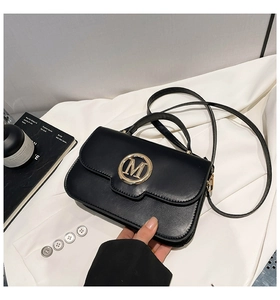 Détail du sac à main en cuir mat noir avec boucle dorée en M et bandoulière amovible