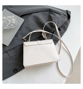 Detail einer strukturierten cremefarbenen Tasche mit Goldbeschlägen auf einem grauen Blazer