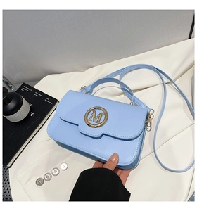 Détail d'un sac à main bleu clair avec logo M doré et bandoulière sur tissu blanc