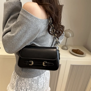 Elegant black shoulder bag with gold chain strap shown on a model in a minimalist setting