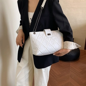 White quilted tote bag with metal chain strap and turn-lock closure on black suit model