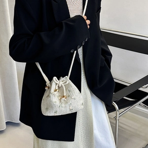 Mini woven bucket bag with green floral embroidery and drawstring, shown on model