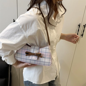 Pink and blue plaid handbag with brown bow detail shown on shoulder in a lifestyle setting
