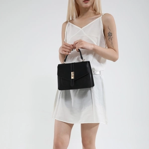Elegante schwarze Lederhandtasche mit goldenem Schloss, getragen zum weißen Kleid