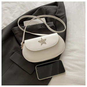 Gros plan d'un sac selle blanc crème avec une étoile en strass argentés sur tissu gris