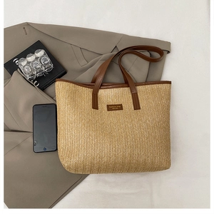 Détail du sac cabas en paille avec anses en cuir marron sur un blazer beige de fond