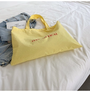 Detail of a bright yellow canvas tote bag with red lettering on a clean bed surface