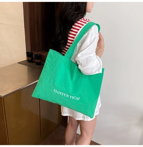 Detail of green nylon tote bag with white letter print and wide shoulder strap