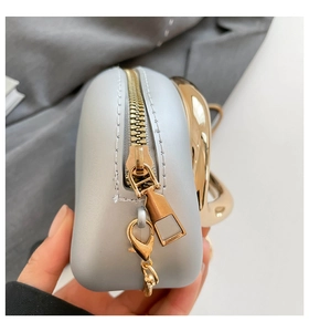 Close-up of light grey box bag featuring gold zipper and metallic ring handle detail
