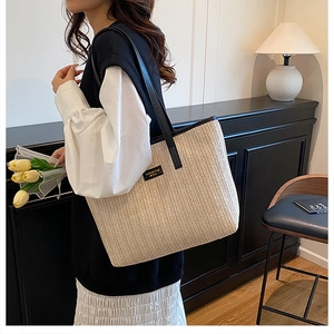 Vue détaillée d'un sac cabas en paille tissée beige avec anses en cuir noir et étiquette mode