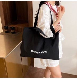 Black nylon tote bag with white lettering showing large capacity on model shoulder