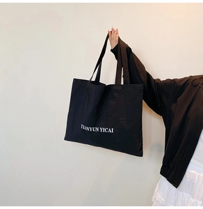 Detail of black large capacity nylon tote bag with TIANYUN YICAI print held by a person